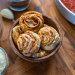 Fresh hot Vegan Pepperoni Pizza Rolls in a wooden bowl on a butcher block counter surrounded by delicious whole food ingredients.